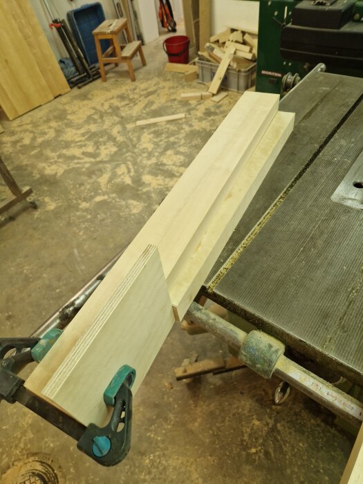 Trästycken kläms ihop på ett arbetsbord i en verkstad, omgivna av sågspån och verktyg.