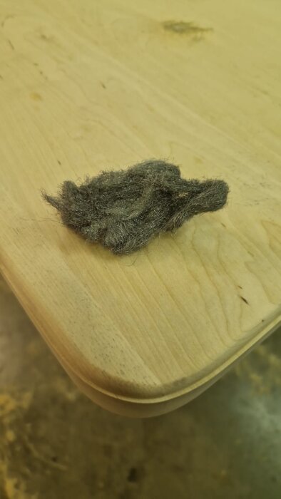 Björkplank med avrundat hörn och bit ståluppull placerad ovanpå som håller på att bearbetas till ett köksbord.