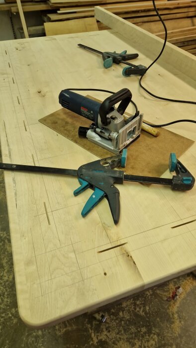 Arbetsbänk med träplanka, limfogar och verktyg som fräs och tvingar för att tillverka köksbord i björk.