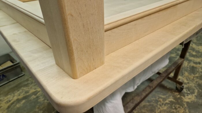 Närbild av ett hörn på ett träbord med rundade kanter, visar benet och sargen i ljust trä med jämn och slät yta.