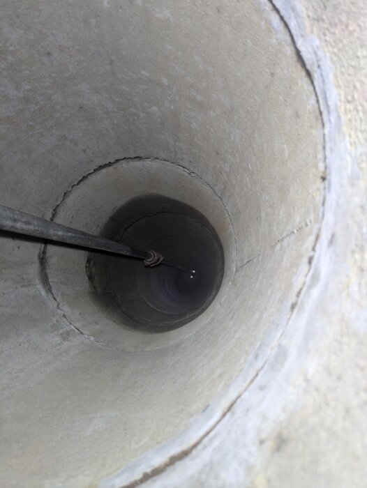 Brunnens insida med synligt vatten cirka 6 meter ner, visar reflektion och fuktighet på väggen vid 1,5 meter djup.