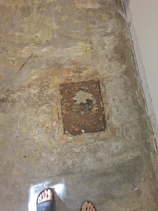 Försänkt plastbrunn med metallock i ett källargolv, omgiven av betong och spår av gammal plastmatta, avslöjad under renovering.