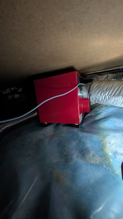 Röd Corroventa 300tt2 avfuktare installerad i krypgrund med plastbeklätt golv och ventilerad våtluftsslang ansluten.
