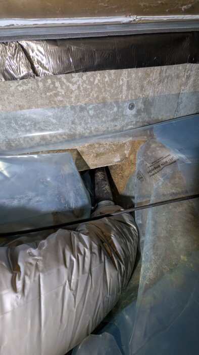 Ventilationsrör i krypgrund, omgärdat av plastduk och tätningsmaterial, med fokus på jordytan och överlappande plastfolie.