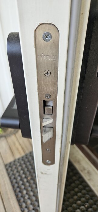 Närbild på en dörr med ett installerat Nimly lås i dörrkarmen, vilket verkar orsaka problem med dörrens täthet.