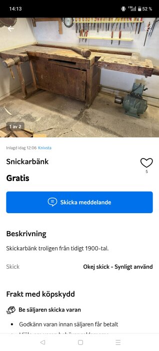 Äldre snickarbänk i trä med skruvstäd och verktygshylla fylld med verktyg, placerad mot en vit vägg på betonggolv.