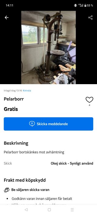 Gammal pelarborrmaskin i ett garage eller verkstad, med fönster i bakgrunden och diverse verktyg och material liggande runt omkring.