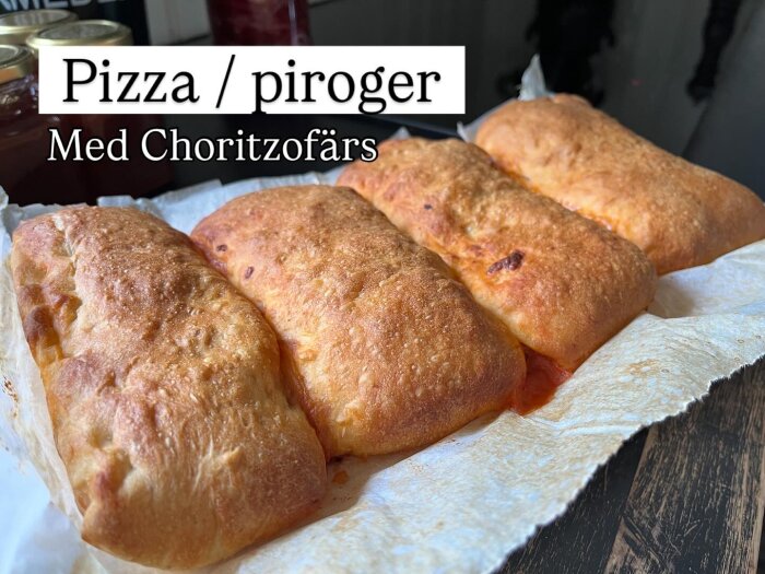 Fyra gyllene piroger på bakplåtspapper, märkta som "Pizza/piroger med chorizofärs", sannolikt fyllda med mozzarella och tomatsås.