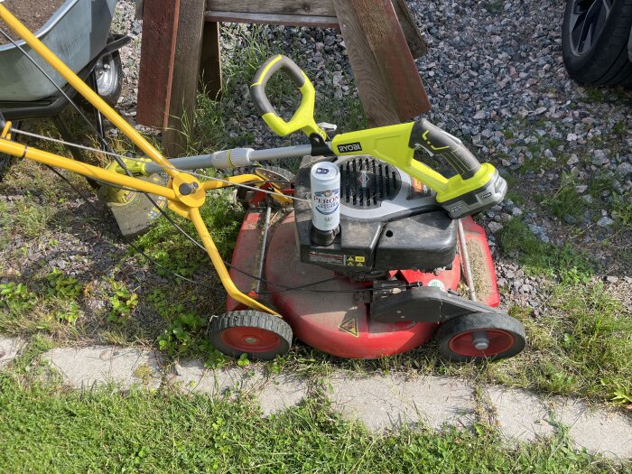 Gräsklippare och grästrimmer med en ölburk placerad på klipparen, omgiven av gräs och grus.