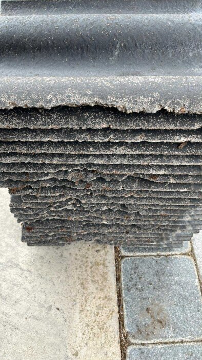 Närbild av staplade, slitna Benders Palema-takpannor från 2010 med synliga skador och slitage.