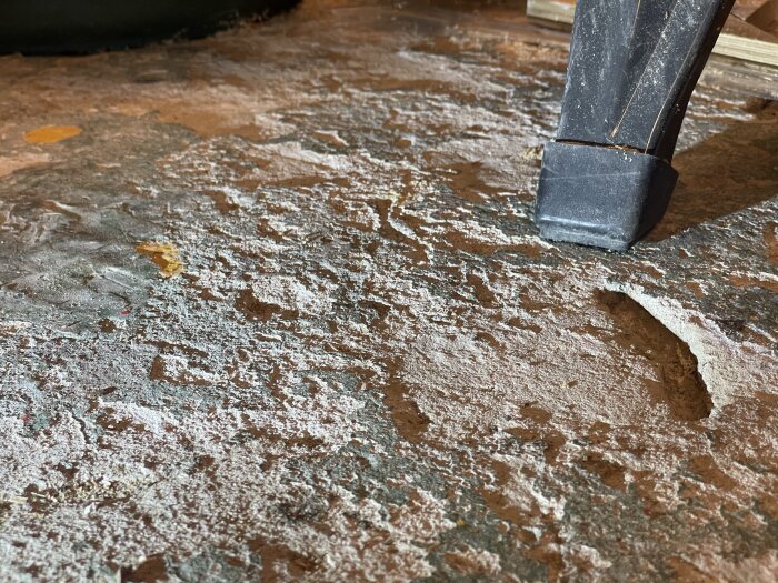 Slitet garagegolv med ojämnheter och repor, belyst med släpljus, visar färgslitage och stora hack i betongen.