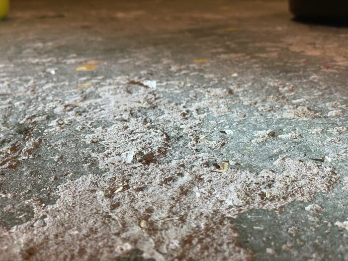 Grovt och slitet garagegolv med färgrester och hack, fotograferat med släpljus för att visa ytan tydligt.