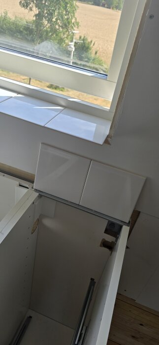 Vitt kakel vid fönsterkarm och köksskåp, del av köksprojekt med mål att uppgradera stänkskyddsområde.