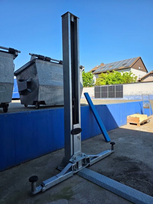 Galvaniserad tvåpelarlyft utomhus bredvid containrar på en betongyta under klarblå himmel.