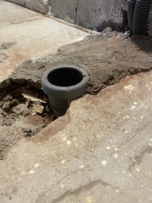 Avloppsrör i betonggolv, med synlig skarv ovanför ytan, i behov av eventuell justering innan golvflytning i köket.