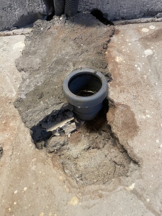 Avloppsanslutning i kök med rörböj strax under golvnivå, omgiven av skadat betonggolv med synliga rör och smuts.