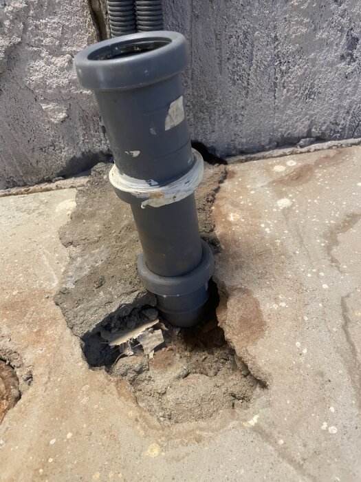 Grått avloppsrör synligt genom golv med spricka runt om, i ett kök under renovering. Röret behöver justeras för att passa golvnivån.