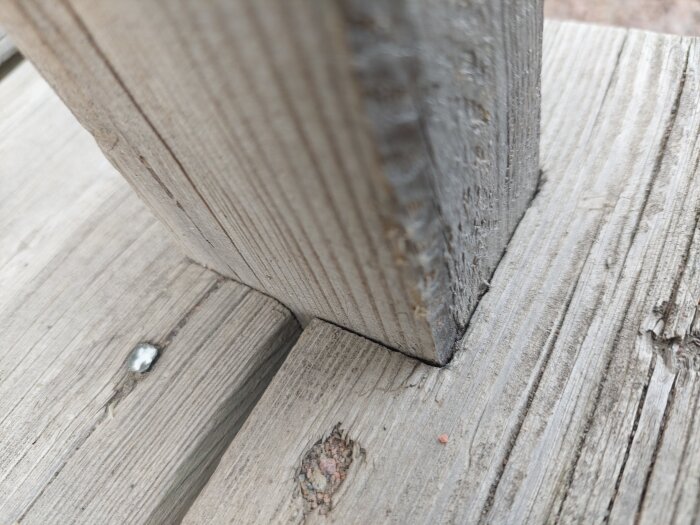 Sliten infästning av trappräcke i impregnerad trätrappa, detaljer av skruv och trästruktur synliga.