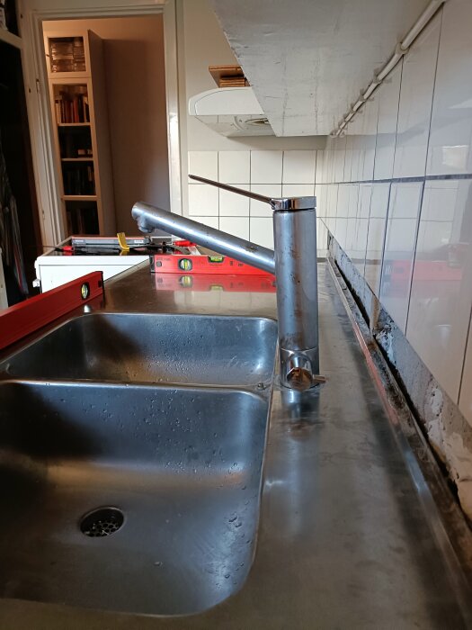 Kök med diskbänk och blandare som justerats med träbit, inredning synlig i bakgrunden; en pågående renovering.