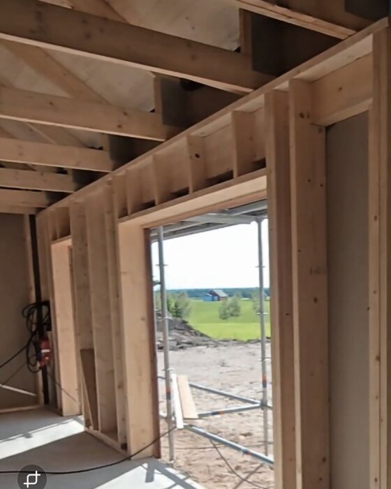 Trästomme i byggnadskonstruktion med exponerade reglar och öppningar för fönster, omgärdat av byggnadsställningar utanför.