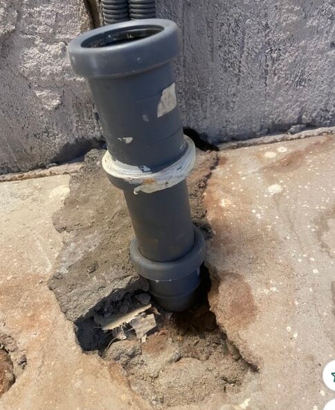 Grått avloppsrör genom betonggolv med flytspackel runt, sett från sidan. Rördelar och tätningar synliga.