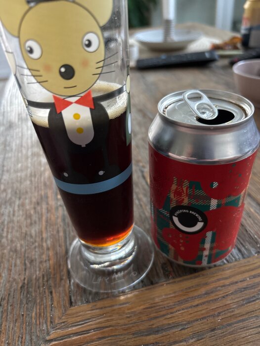 Ett glas med Ale från Nyköping Brewing och en ölburk på ett träbord.