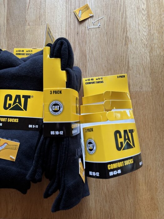 Svarta strumpor från CAT, förpackade i gula kartonger. Tre paket syns, med etiketter i olika storlekar på golvet.