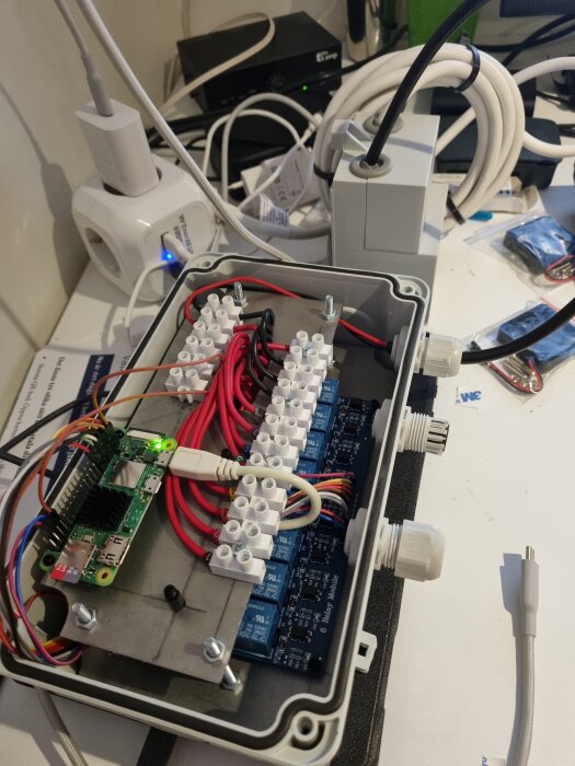 Öppen kopplingsdosa med elektronik och sladdar på skrivbord, ansluten till ström.
