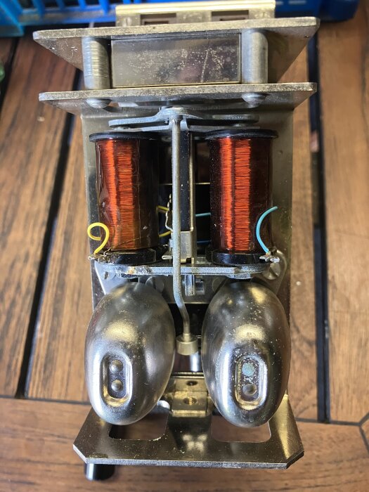 Ringtång med två metallklockor och kopparlindningar, misstänkt som en ringklocka som kanske kräver ström eller manuell vevning.