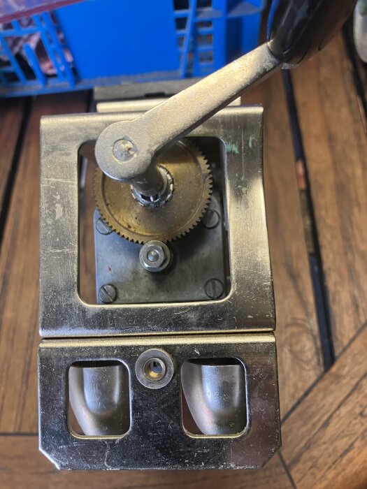 Manuell ringklocka med vev och synliga kugghjulsmekanismer, monterad på träytan.