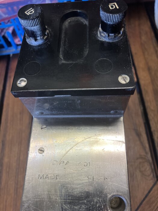 Svart mekanisk apparat med två vred märkt med "DPA 101 MADE IN SWEDEN" på metallplatta, troligen en manuell ringklocka.