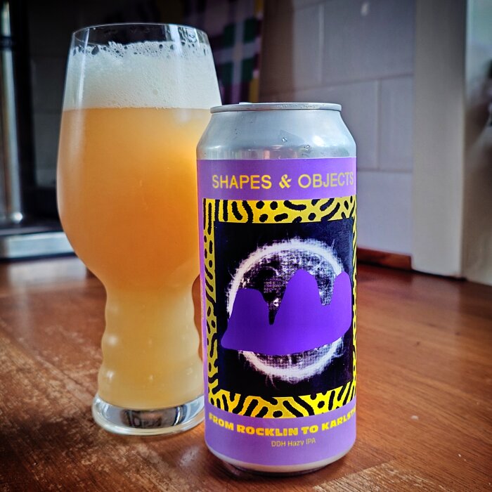 En burk "Shapes & Objects" DDH Hazy IPA och ett glas med orangefärgad, skummande öl på ett bord.