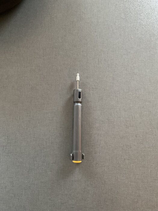 En grå låddämpare ligger på ett mörkt tygunderlag.