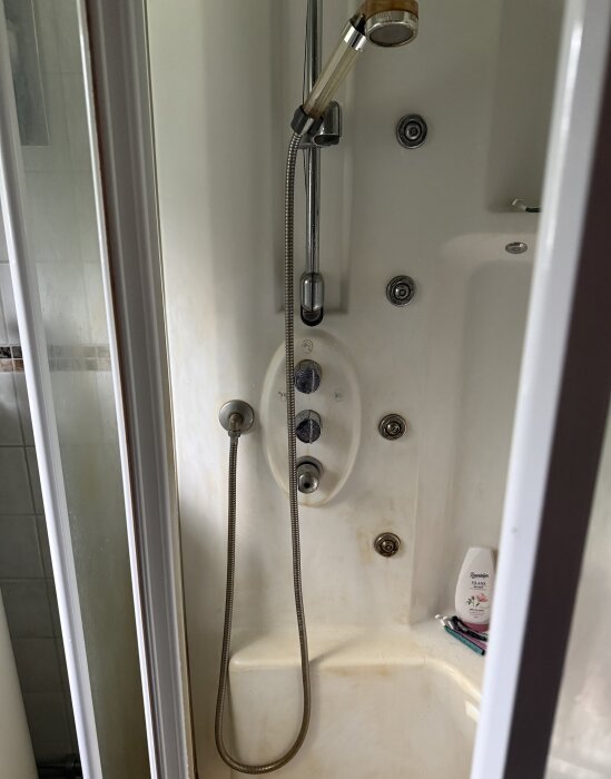 Duschkabin med duschmunstycke, reglage och några tvättprodukter synliga i duschens internitat.