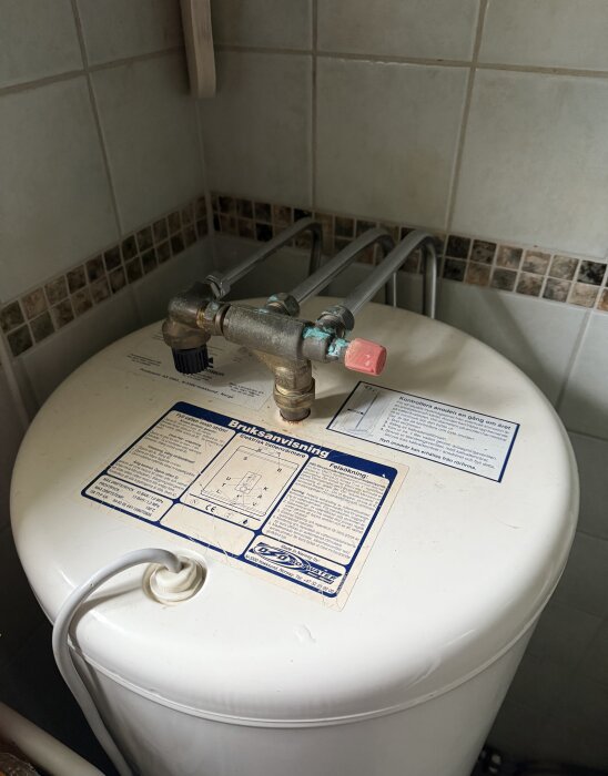 Varmvattenberedare med anslutna rör och instruktioner på locket.