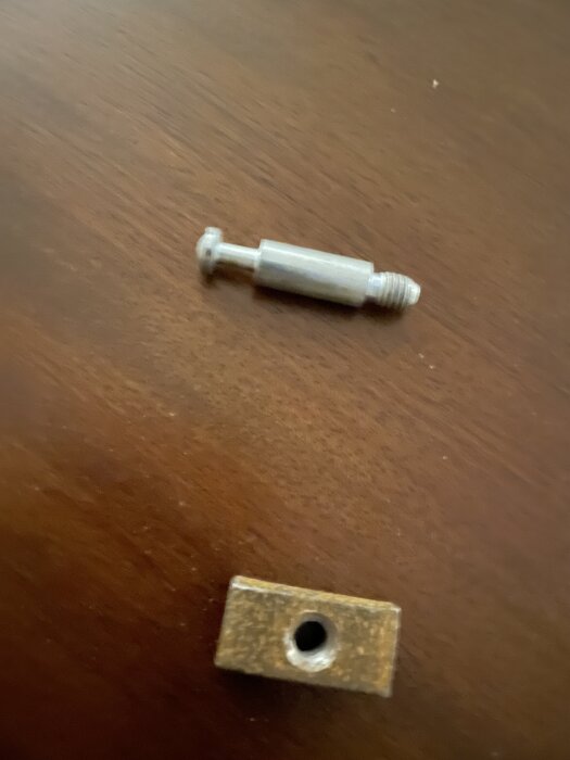 Skruv och mutter liggande på en träyta, del av ett bokhyllans montage som saknar fler komponenter.