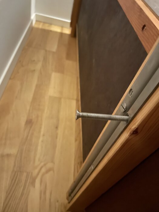 En träbokhylla under montering med en lång, silverfärgad skruv delvis isatt i en sidopanel.