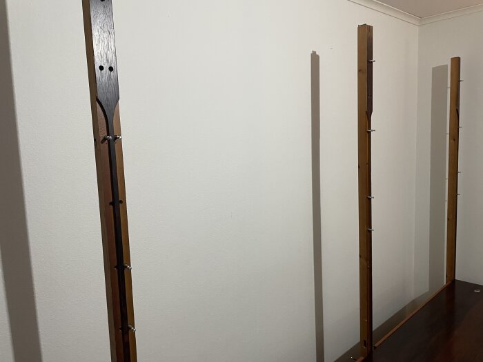 Trästolpar på en halvmonterad bokhylla med skruvar synliga, placerad mot en vit vägg i ett rum.