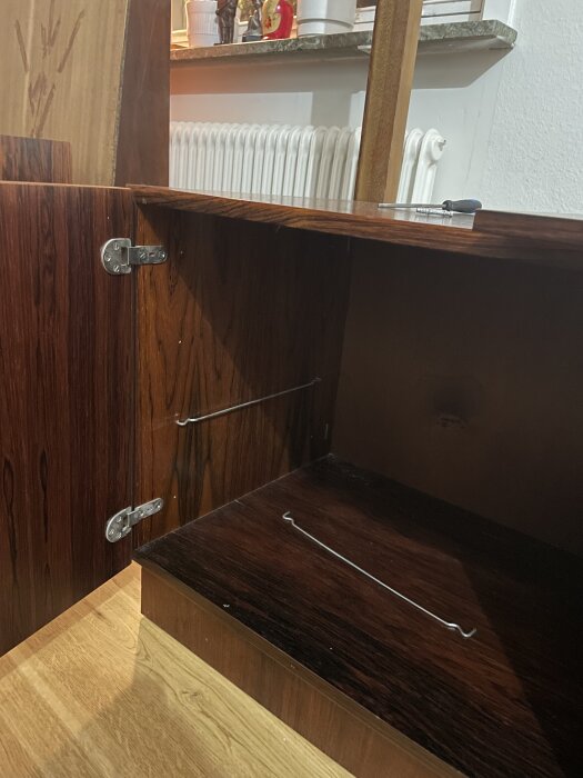 En öppen bokhylla med två gångjärn, träluckor och trådhyllor, förberedd för montering; saknade skruvar och muttrar.