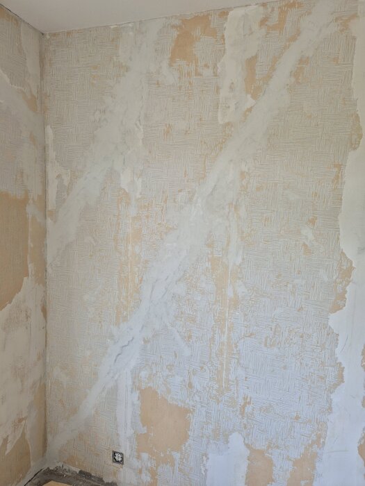 Vägg med cementbaserat spackel där sprickor i betong försökts fyllas, synbart ojämnt resultat och synliga strukturer i gipsväggen.