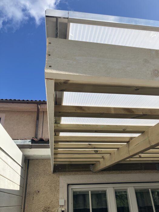 Kanalplasttak ovanför en altan med synlig trästomme och överhäng, integrerat med ett äldre hus där taket går i linje med ramen.