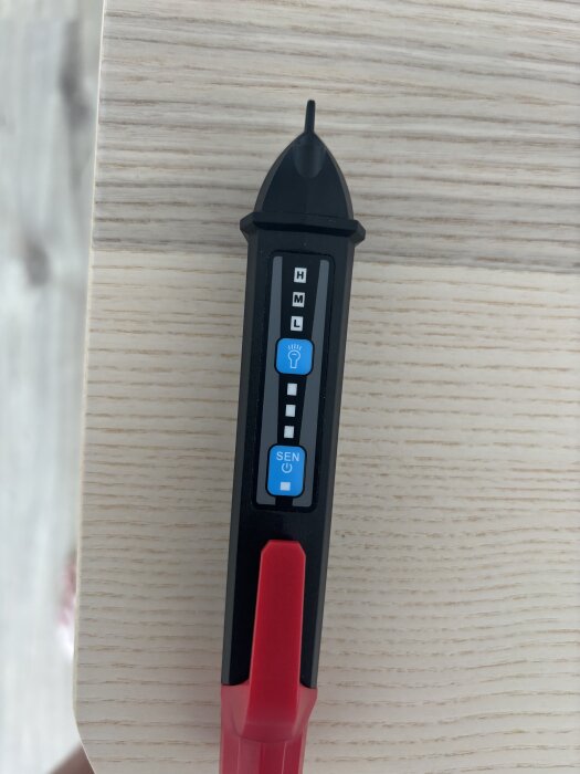 Verktyg med inställningar för hög, medel och låg känslighet, och en strömbrytare, placerat på en träyta.