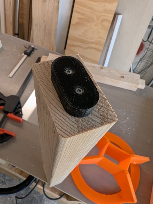 Träregel med 3D-utskrivet svart plastfäste monterat på toppen, omgiven av träplankor och verktyg.
