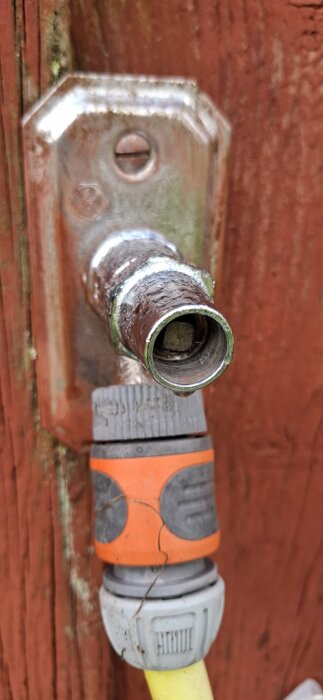 Slitet Vårgårda Amartur från 1983 monterat på röd vägg, med fyrkanttapp och kopplat vattenslangfäste i orange och grått.