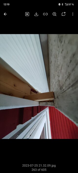 Klädd takfot med vit panel över röd träfasad och träbjälkar, del av sjunkande uterum.