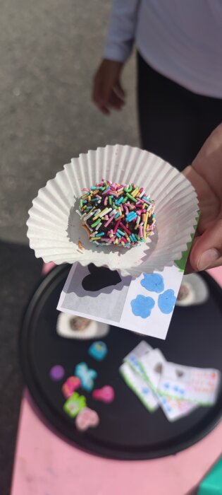 Hand håller en muffinsform med färgglada strössel på chokladöverdrag.