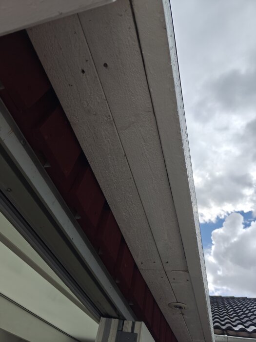 Takfot av uterum sedd från undersidan med demonterad bräda, visar insidan och uppvisar tidigare klädd yta. Mulen himmel i bakgrunden.