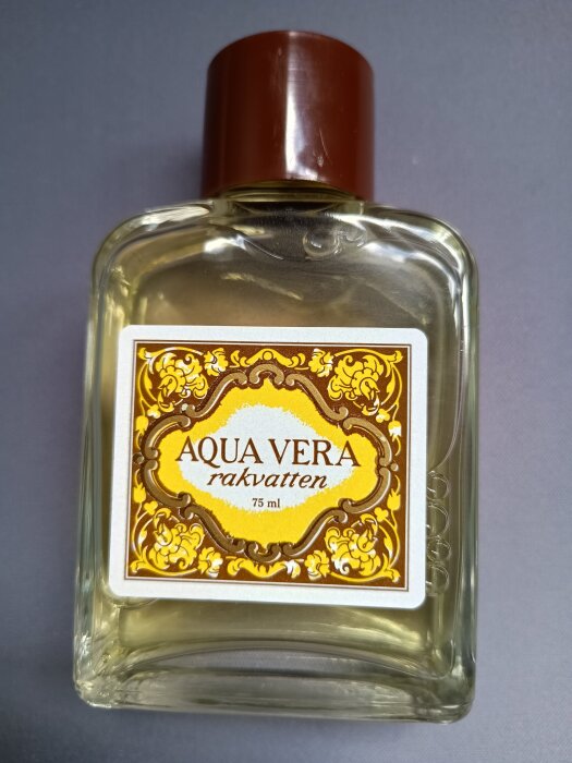 Flaska med Aqua Vera rakvatten, 75 ml, med en etikett i gul och brun dekor. Känd för sin citrusdoft.