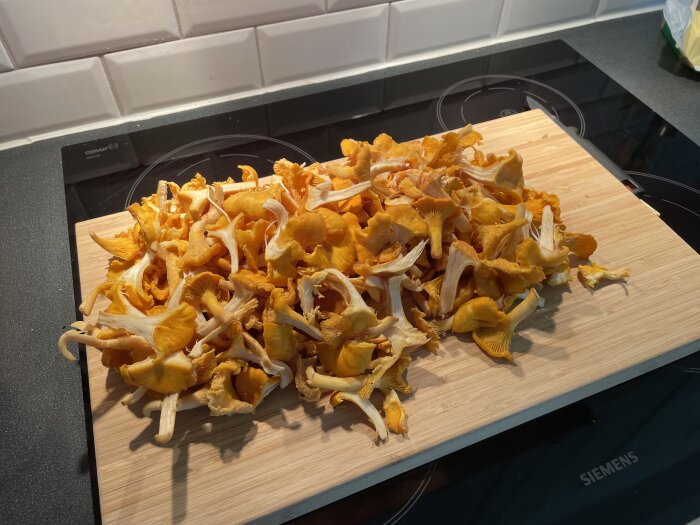 Färska kantareller på en skärbräda, redo att tillagas, med en modern spis i bakgrunden.