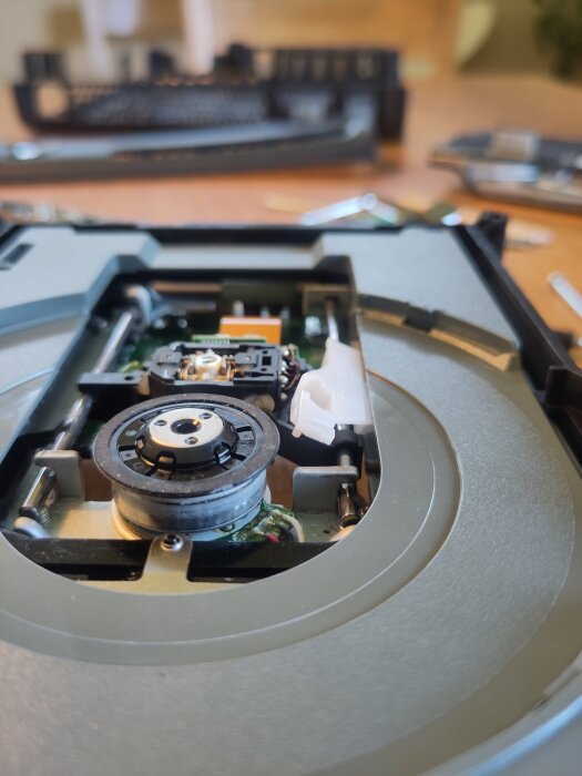 Inuti en Xbox 360 där laserskivan är synlig, med en vit plastbit som inte sitter rätt. Verktyg och delar i bakgrunden tyder på reparation.